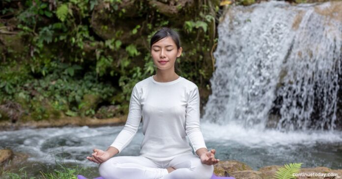 An women meditating in front of a waterfall to improve spiritual health